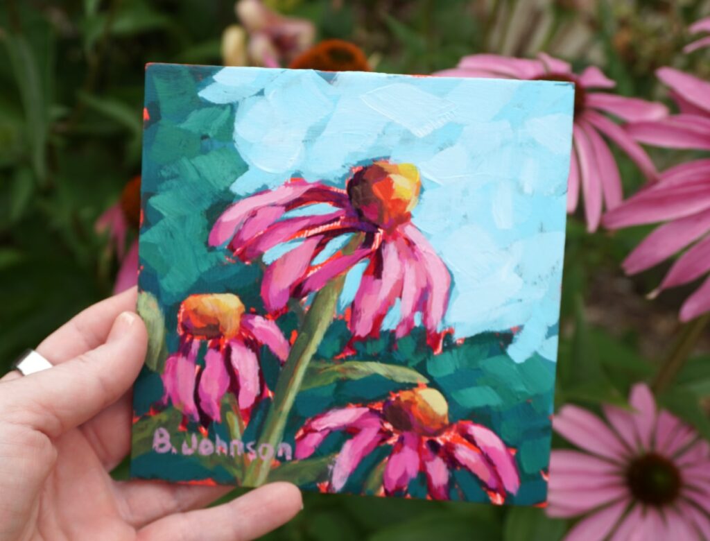 an acrylic painting of coneflowers held in front of a garden of coneflowers